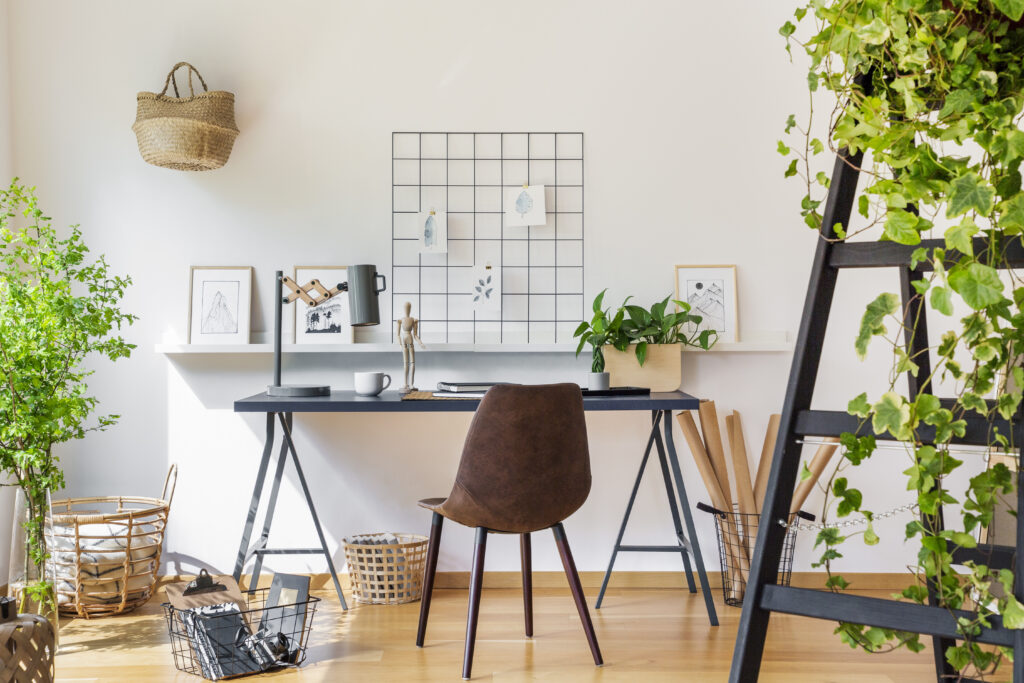 brown chair at desk in white boho home office interior with plants and posters real photo